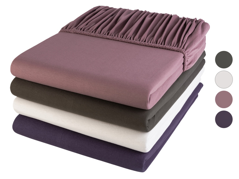 Een stapel van vier hoeslakens in verschillende kleuren: roze, donkergroen, wit en paars.