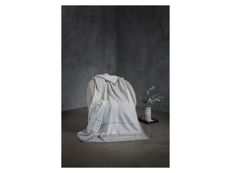 Grijs-witte plaid op een fauteuil, met een vaas met groen ernaast.