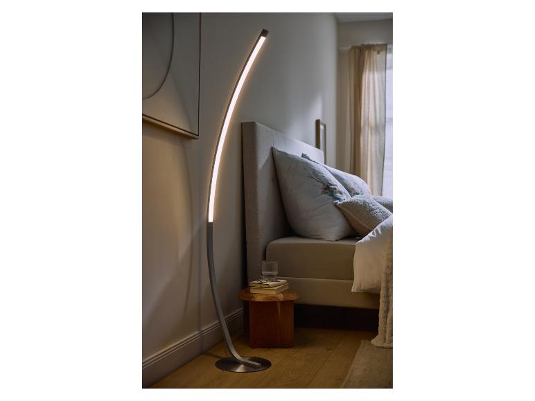 Gebogen LED vloerlamp verlicht een moderne slaapkamer met bed en nachtkastje.