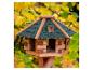 Houten vogelhuisje met groen dak en gele herfstbladeren op de achtergrond.