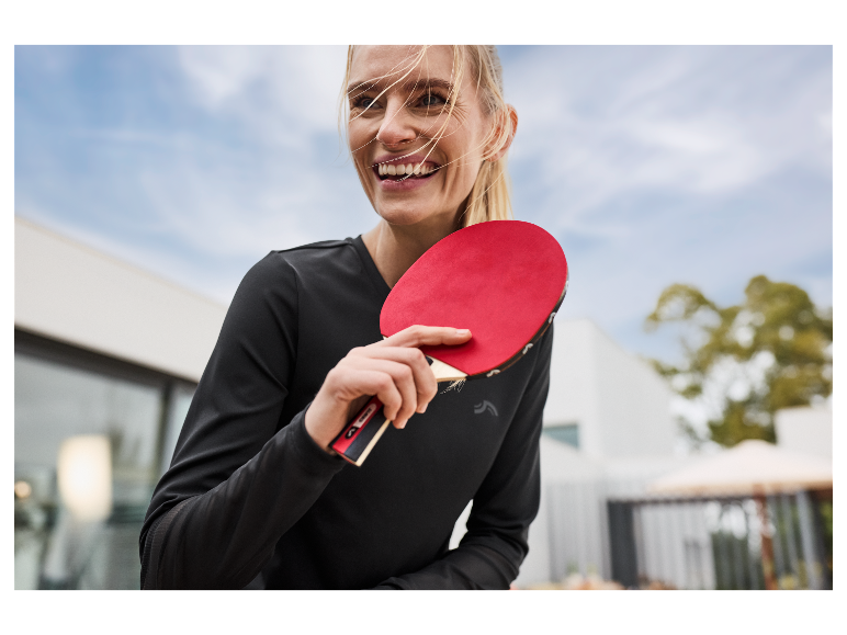 Een lachende vrouw houdt een rode tafeltennisbat vast.