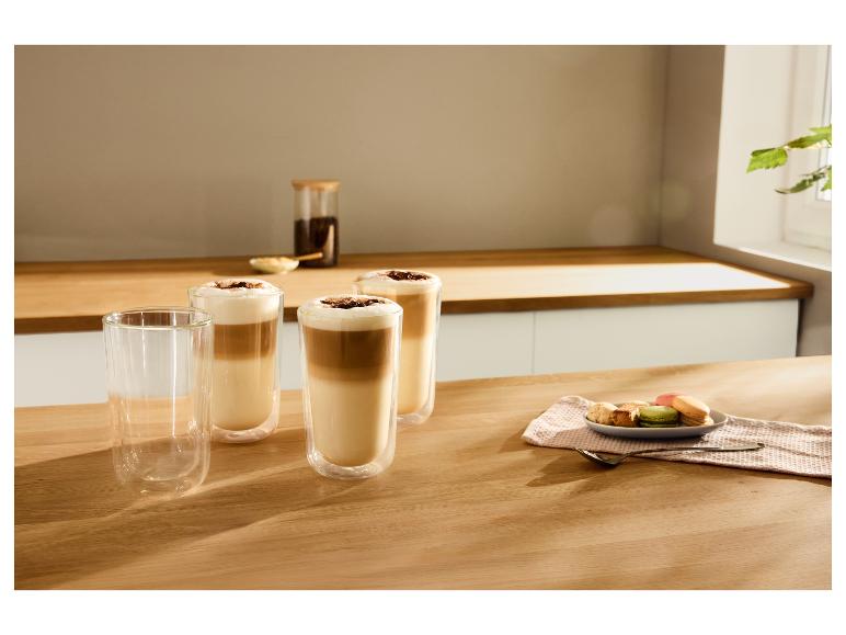 Drie glazen koffielatte met schuim en chocoladeschilfers, naast macarons en koekjes.