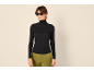 Vrouw in zwarte coltrui en groene broek, zonnebril.