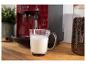 Koffiezetapparaat schuimt melk op in een glazen mok, met een pot koffiebonen ernaast.