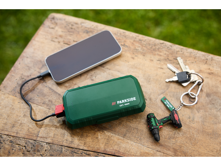 Groene powerbank laadt smartphone op, met sleutels en mini-boormachine sleutelhanger.