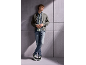 Jonge man in grijs jack, jeans en sneakers, leunend tegen een muur.
