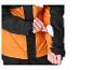 Hand stopt een witte kaart in een zak met rits op de mouw van een oranje en zwarte jas.