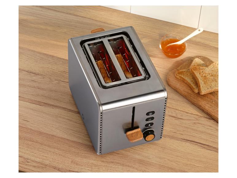 Roestvrijstalen broodrooster met houten accenten, toast en jam op een houten aanrecht.