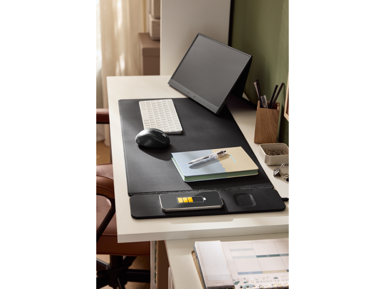 Een modern bureau met een draagbare monitor, toetsenbord, muis, notitieboekje en een opladende telefoon.