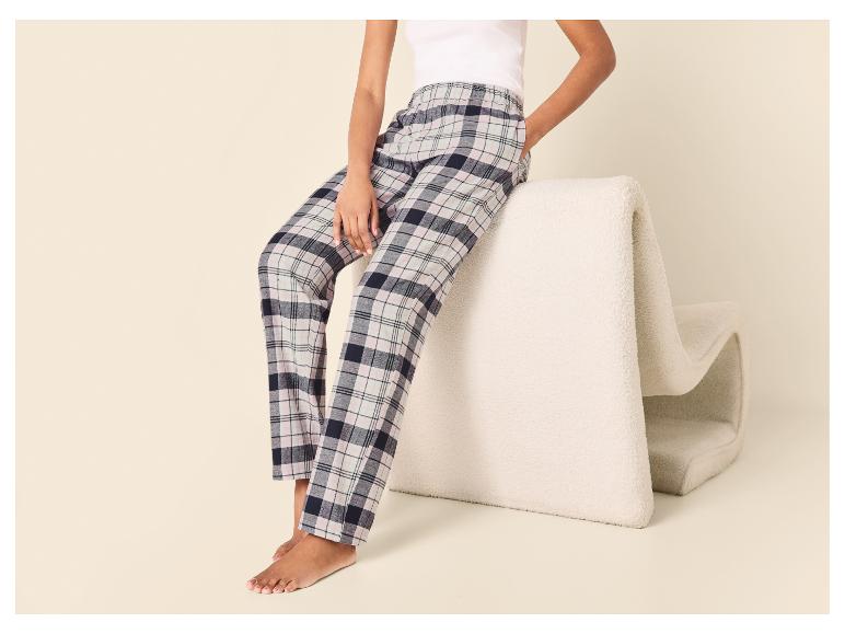 Vrouw zit op een witte stoel met geruite pyjamabroek en witte top.