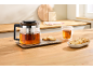 Glazen theepot met thee en koekjes op een houten aanrecht.