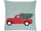 Kussen met rode vrachtwagen die een kerstboom en cadeaus vervoert in de sneeuw.