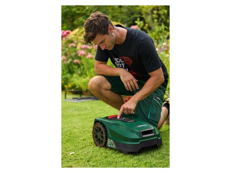 Man knielt op een gazon en stelt een robotmaaier af.