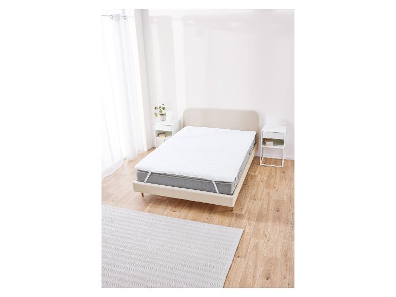 Witte matrasbeschermer op bed in minimalistische slaapkamer.