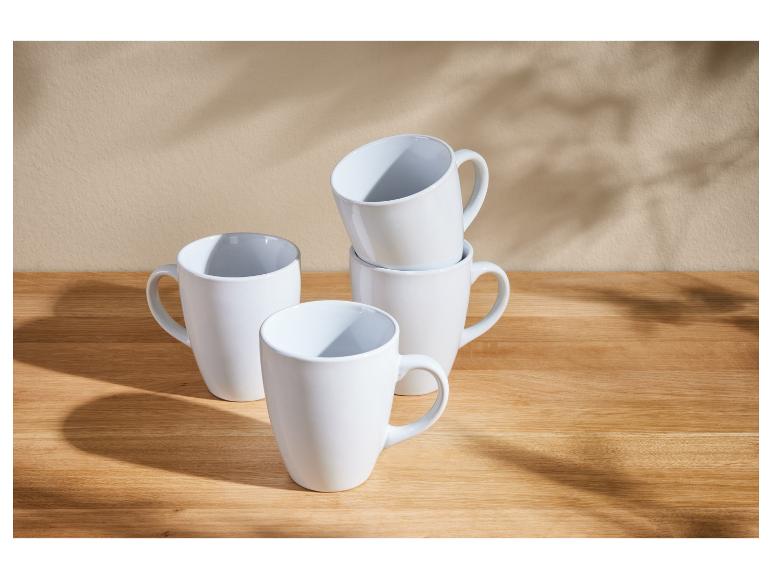 Vier witte mokken op een houten tafel.