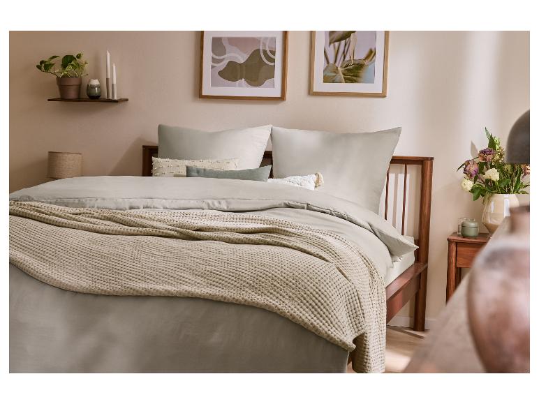 Slaapkamer met een tweepersoonsbed, grijs beddengoed en een getextureerde beige deken.