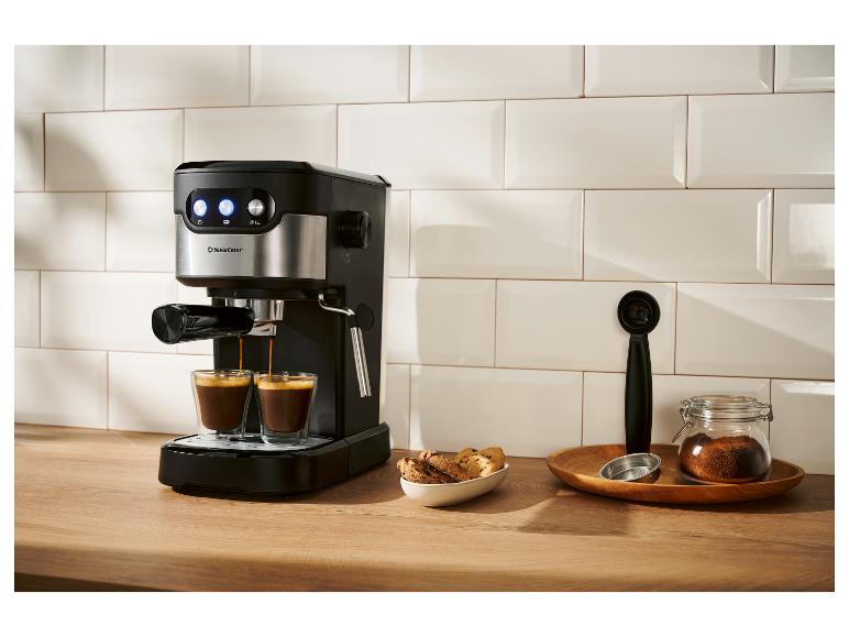Zwart-zilveren espressomachine zet twee kopjes koffie in een moderne keuken.