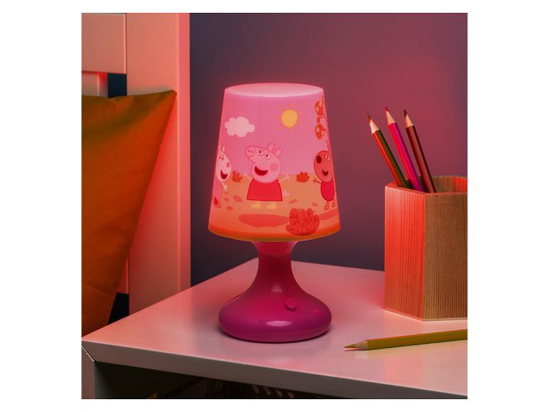 Roze kinderlamp met tekenfilmfiguren en een pot met kleurpotloden op een tafel.