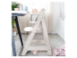 Een lichte houten kinderstoel naast een tafel.