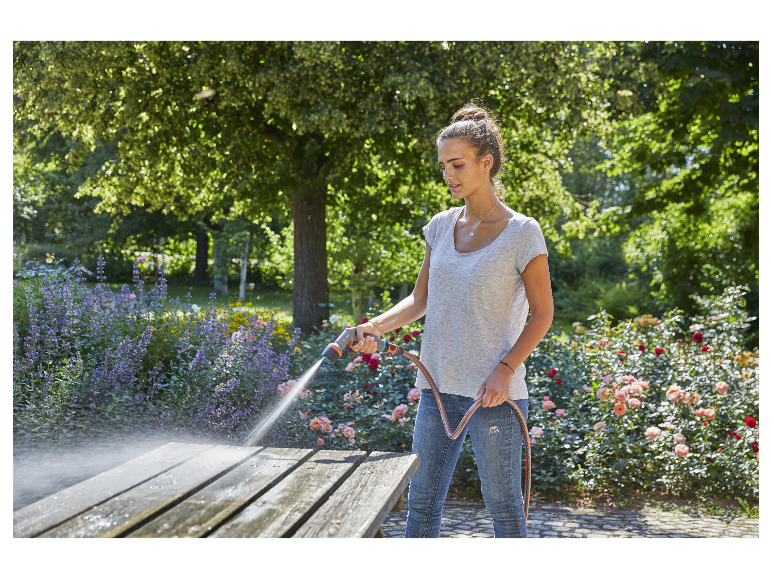 Vrouw reinigt houten tafel met tuinslang in rozentuin.