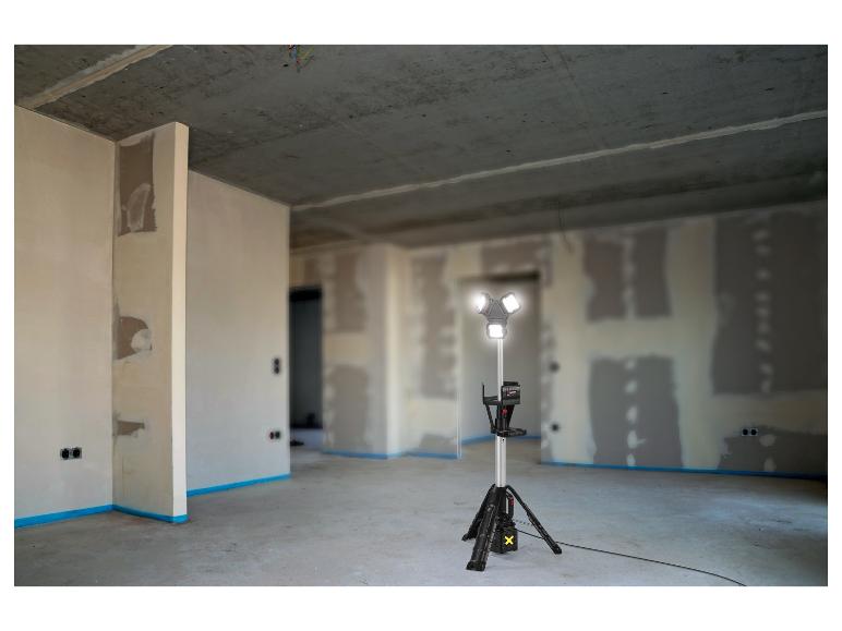 Een bouwlamp op statief verlicht een onafgewerkte kamer met gipsplaatwanden.