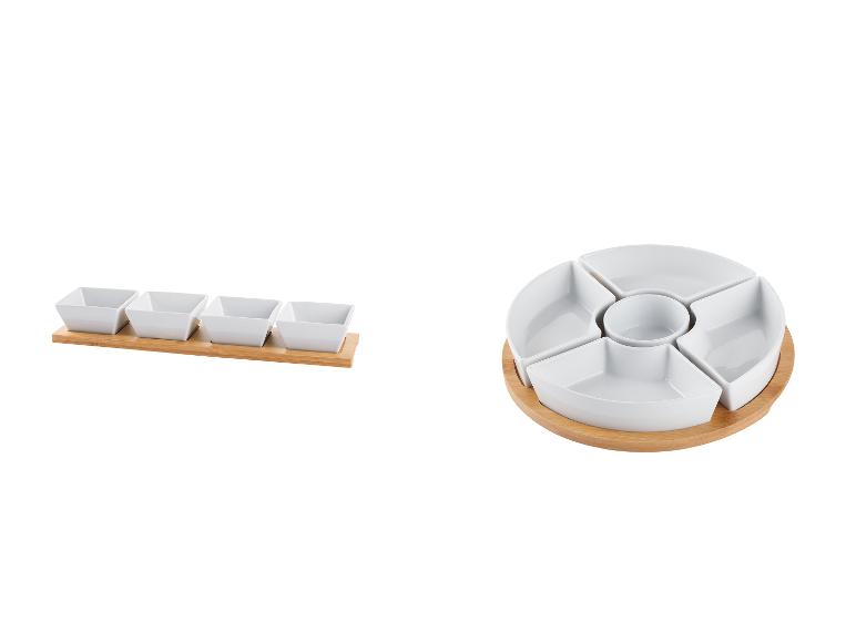 Een ronde en rechthoekige serveerschaal van wit porselein met een houten onderstel.