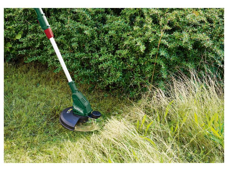 Grasmaaier trimt hoog gras naast een struik.