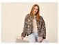 Vrouw in luipaardprint jas en lichte jeans zit op een wit podium.