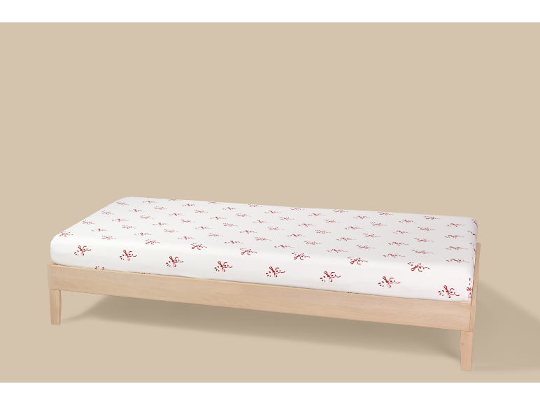 Wit hoeslaken met rood strikjespatroon op een houten bed.