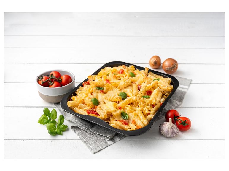 Gebakken pasta met tomaten, basilicum en uien op een witte houten tafel.