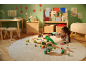 Meisje speelt met houten treinbaan en dinosaurussen op een rond vloerkleed in een kerstkamer.