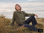 Vrouw in een groene jas en donkere jeans zittend in een grasveld.
