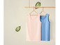 Twee tanktops, een roze en een blauwe met witte stippen, hangen aan houten hangers.