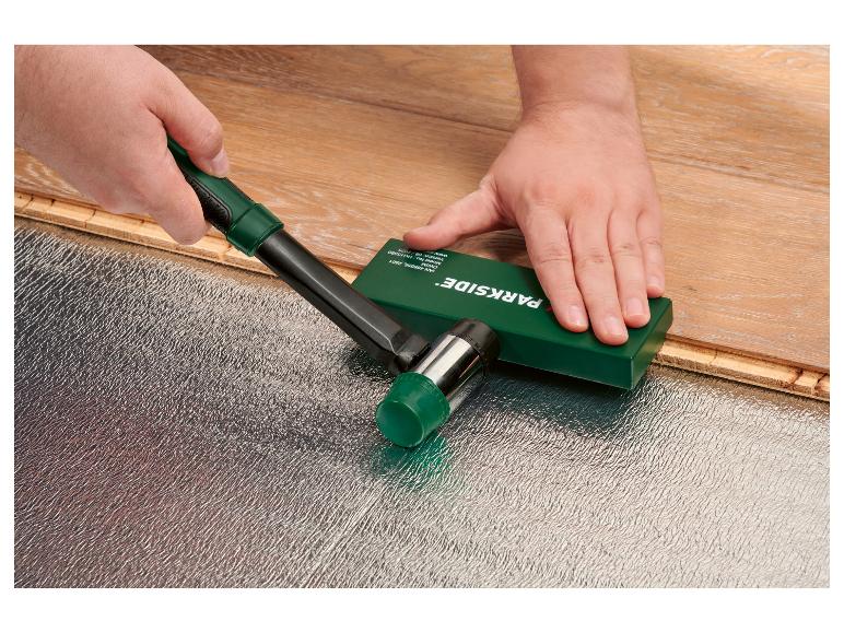 Een werknemer installeert laminaatvloeren met een rubberen hamer en een slagblok.