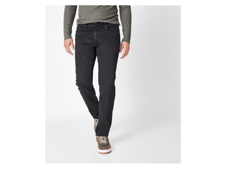 Een man draagt een zwarte jeans en een olijfgroene trui.