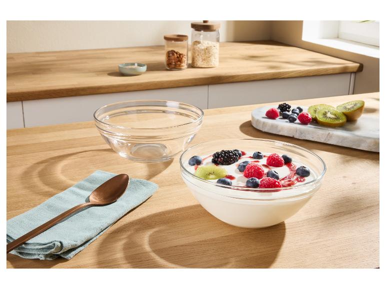 Yoghurt met bessen en kiwi in een glazen kom op een houten aanrecht.