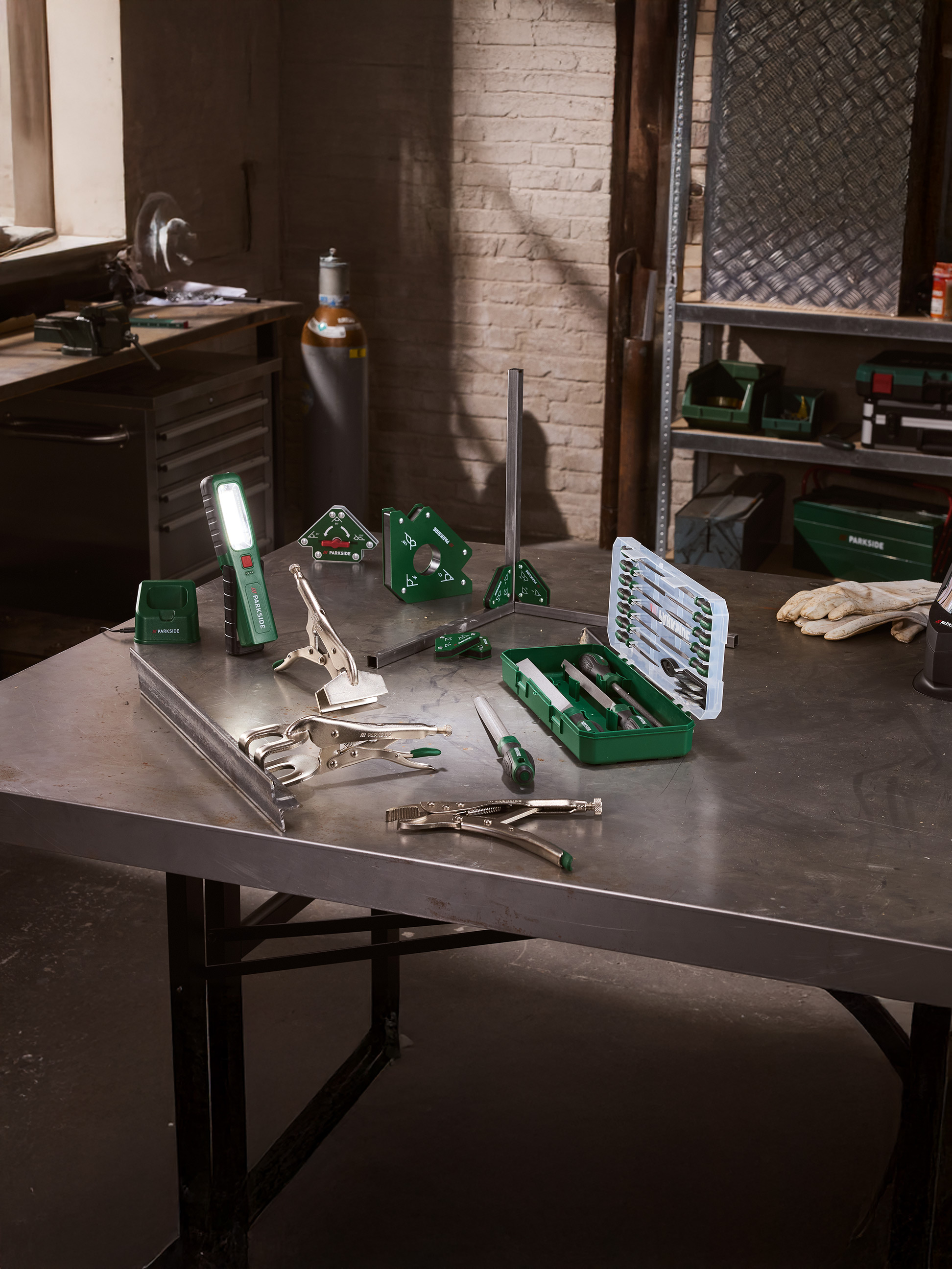 Las- en vijlgereedschap op een metalen tafel in een werkplaats, met een LED-zaklamp.