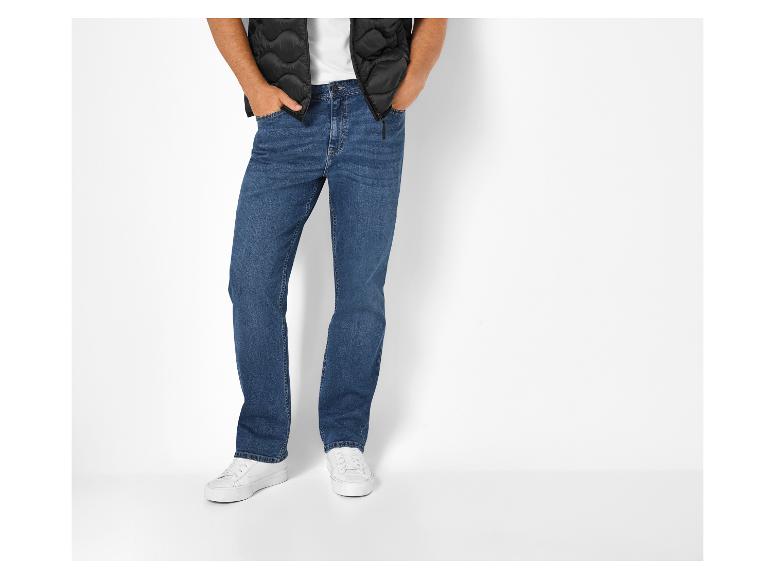 Man in zwart gewatteerd vest, wit T-shirt en blauwe jeans met witte sneakers.