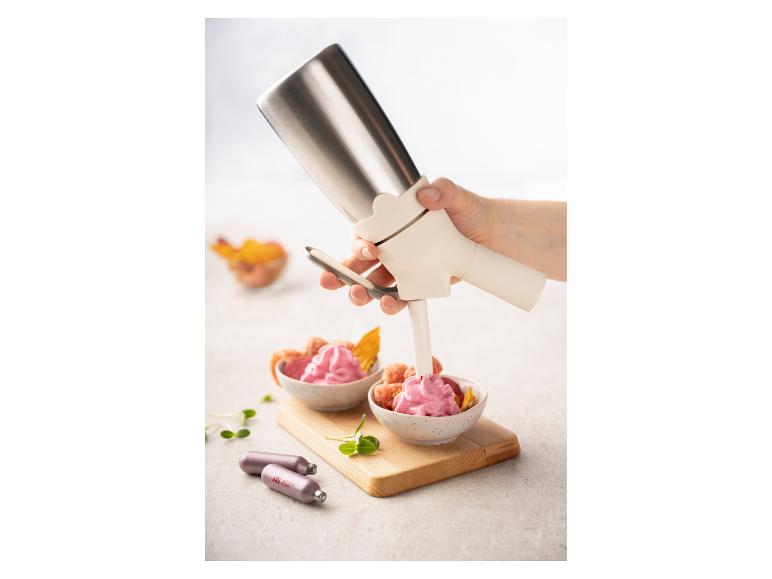 Slagroomspuit vult roze slagroom in een fruitschaal, met patronen op tafel.