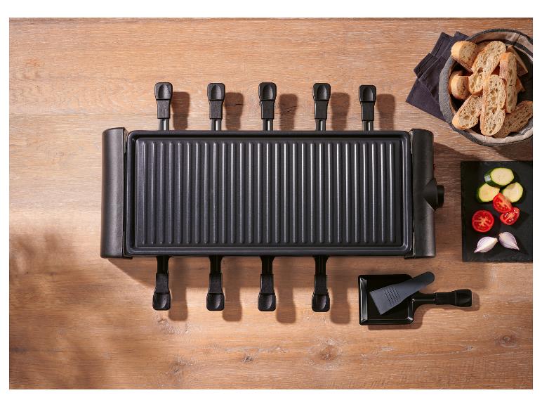 Raclette grill met zes pannetjes, brood en gesneden groenten op een houten tafel.