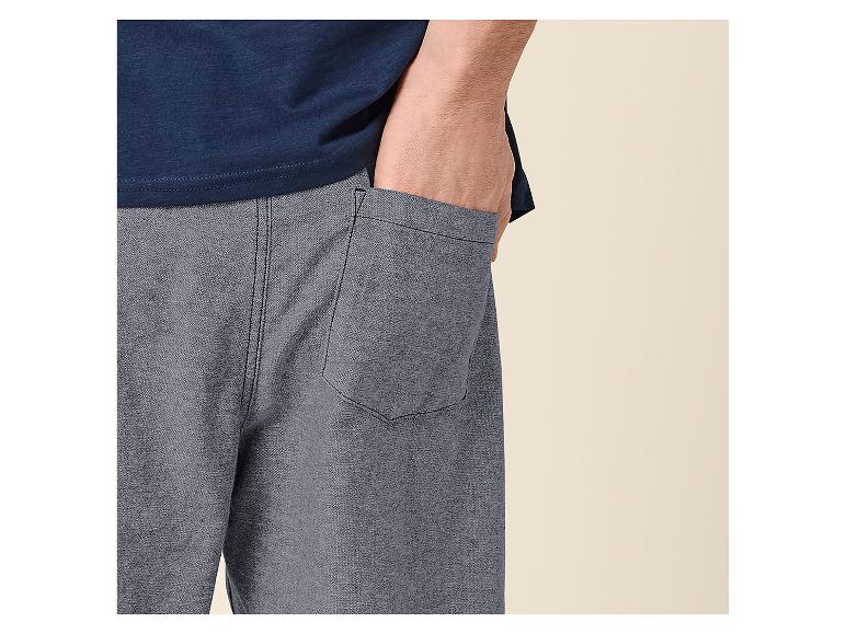 Man in blauw T-shirt en grijze korte broek met hand in zak.