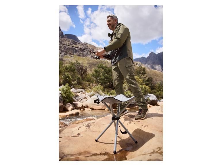 Man vist in bergrivier, draagt kaki jas en broek, met opvouwbaar krukje.