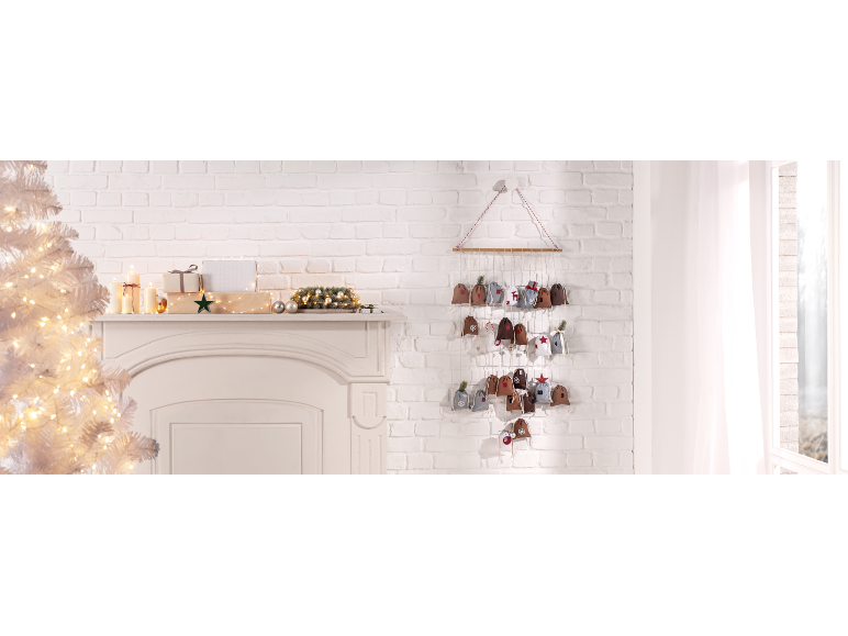 Stoffen adventskalender met kleine zakjes, kerstdecoraties en kaarsen in een feestelijke setting.