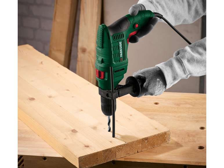 Boormachine in handen boort in een houten plank op een werkbank.