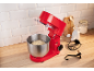 Rode keukenmixer met deeg in een kom, bakingrediënten en accessoires op een houten aanrecht.