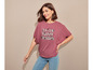 Een vrouw draagt een roze T-shirt met de tekst 'Think Happy Thoughts' en blauwe jeans.
