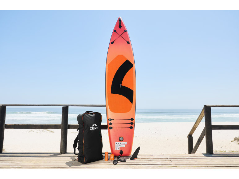 Oranje paddleboard met accessoires en tas op een houten vlonder bij het strand.