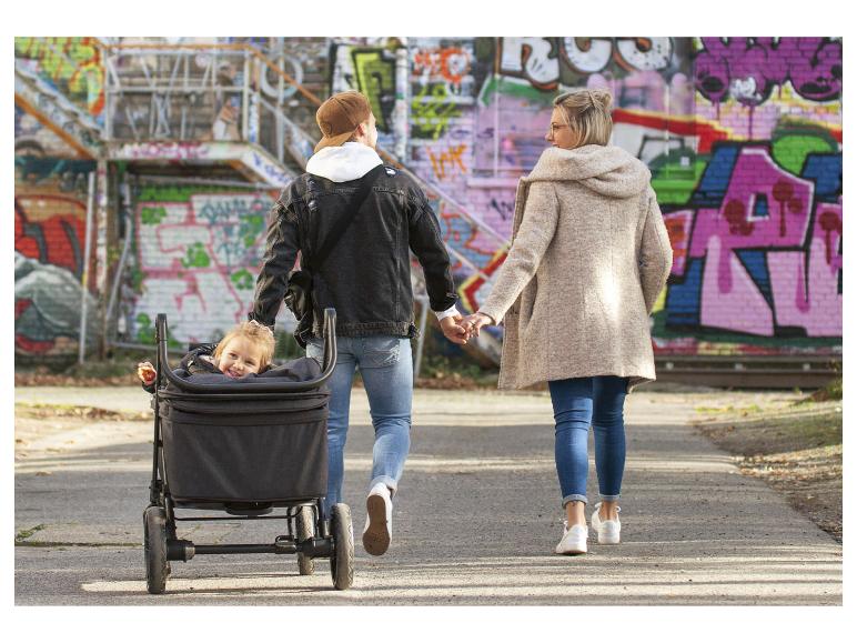 Familie met kind in kinderwagen wandelt hand in hand langs een graffitimuur.