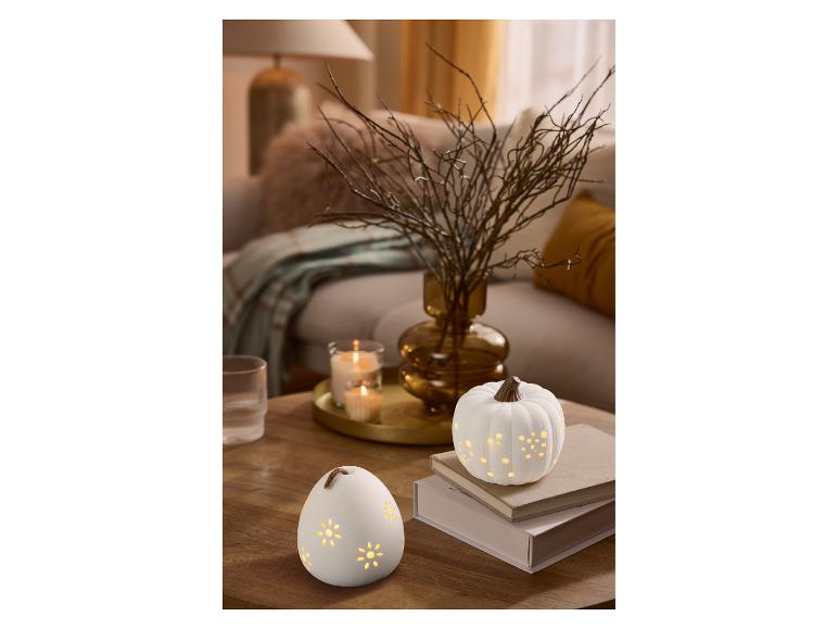 Twee decoratieve lampjes in de vorm van een pompoen en een ei, met bloemmotieven, op een houten tafel.