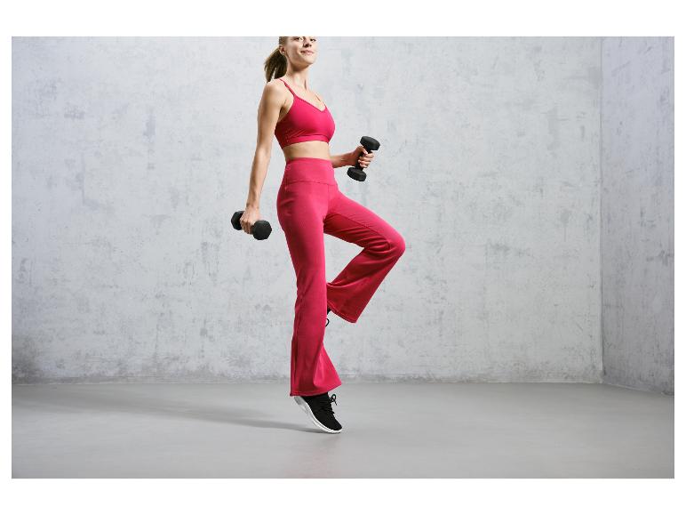Een vrouw in roze sportkleding met haltertop en broek, oefent met dumbbells.